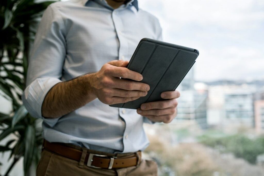 Geschäftsmann betrachtet ein Tablet im Büro vor großer Fensterfront
